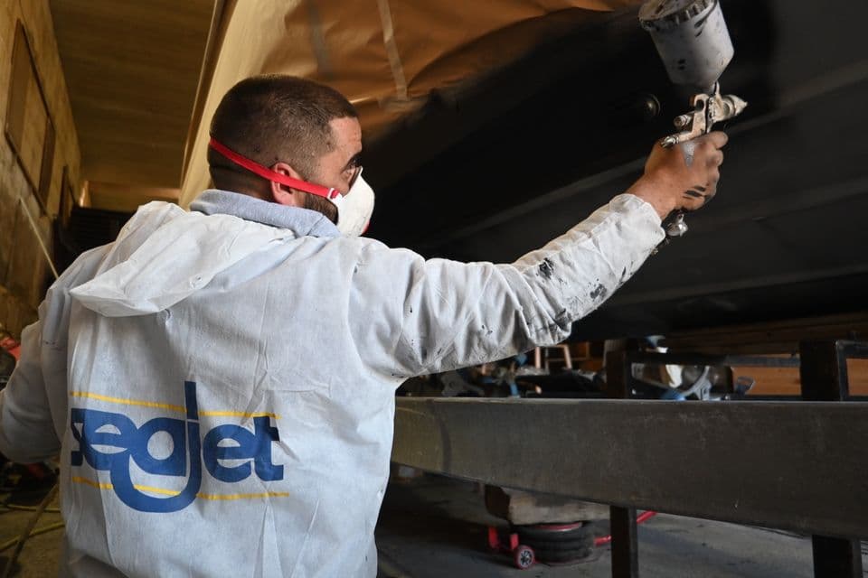 Spraying Seajet antifouling on a hull in a boatyard shed